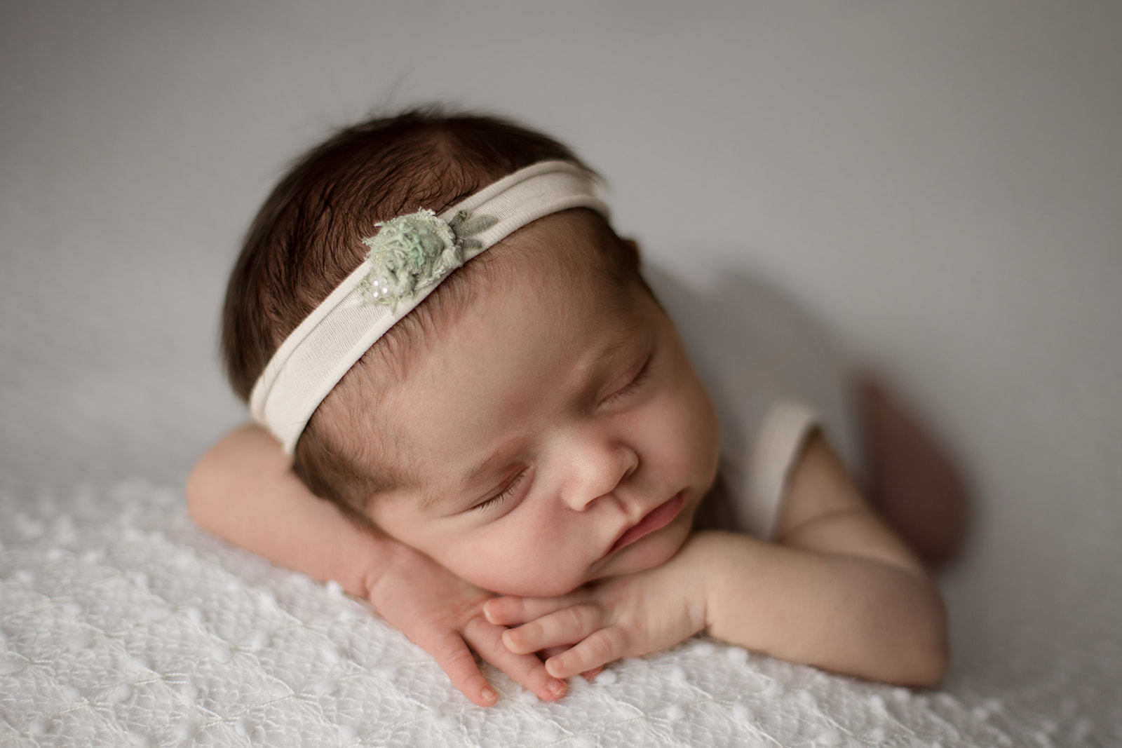 A newborn baby sleeps on her hands in a white headband on a bed after mom got a 3D Ultrasound in Houston