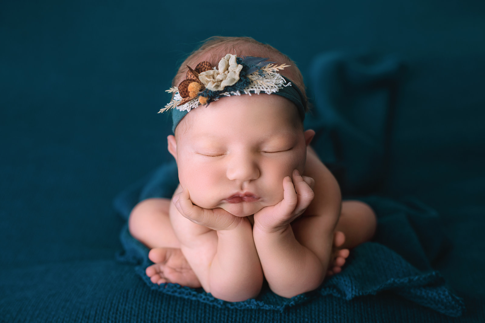 A newborn baby sleeps on her hands on a blue bed in a matching headband thanks to fertility clinic in Houston