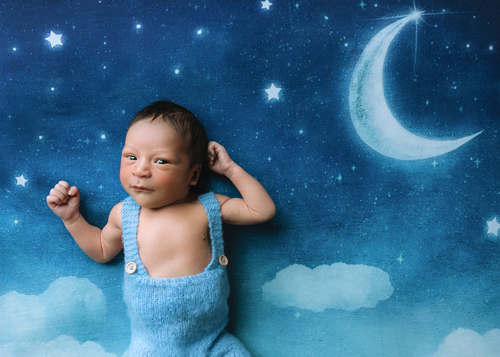 A newborn baby lays on a mat of the moon and stars in blue knit overalls thanks to a fertility clinic in Houston