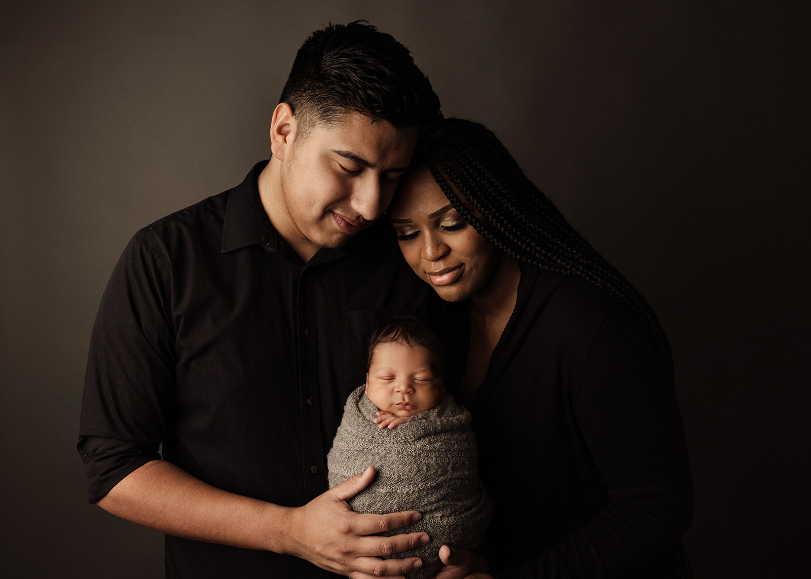 Happy new parents smile down at their sleeping newborn baby in their hands after using Houston Baby Shower Venues