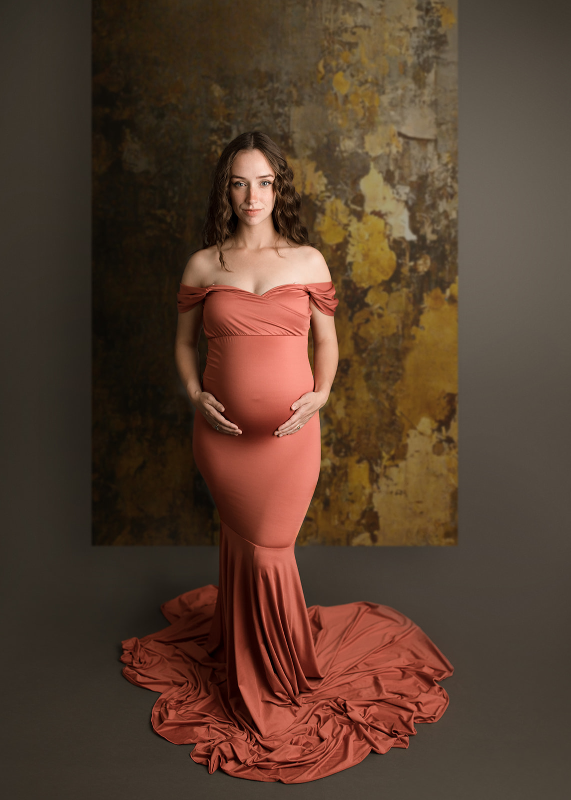 A mother to be stands in a pink maternity gown holding her bump in a studio after visiting a Houston Birthing Centers