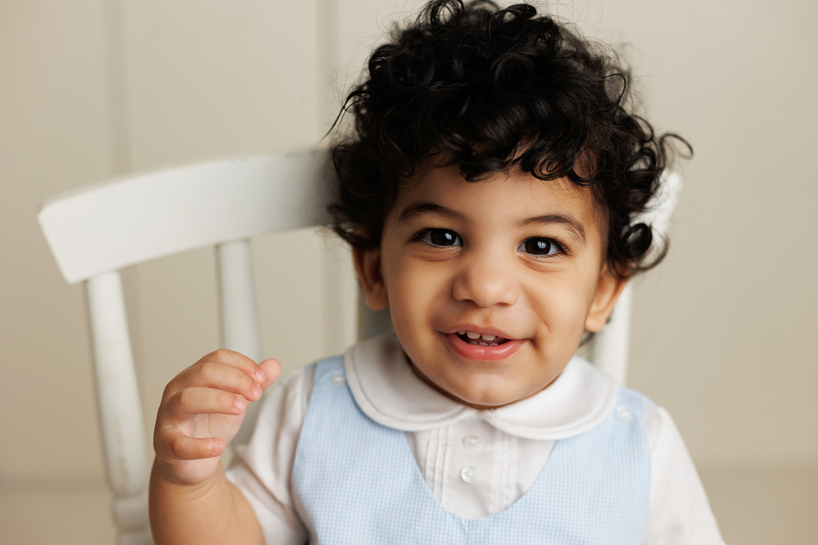 A young boy in a blue vest sits on a wooden chair in a studio with a big smile after visiting Houston Daycares