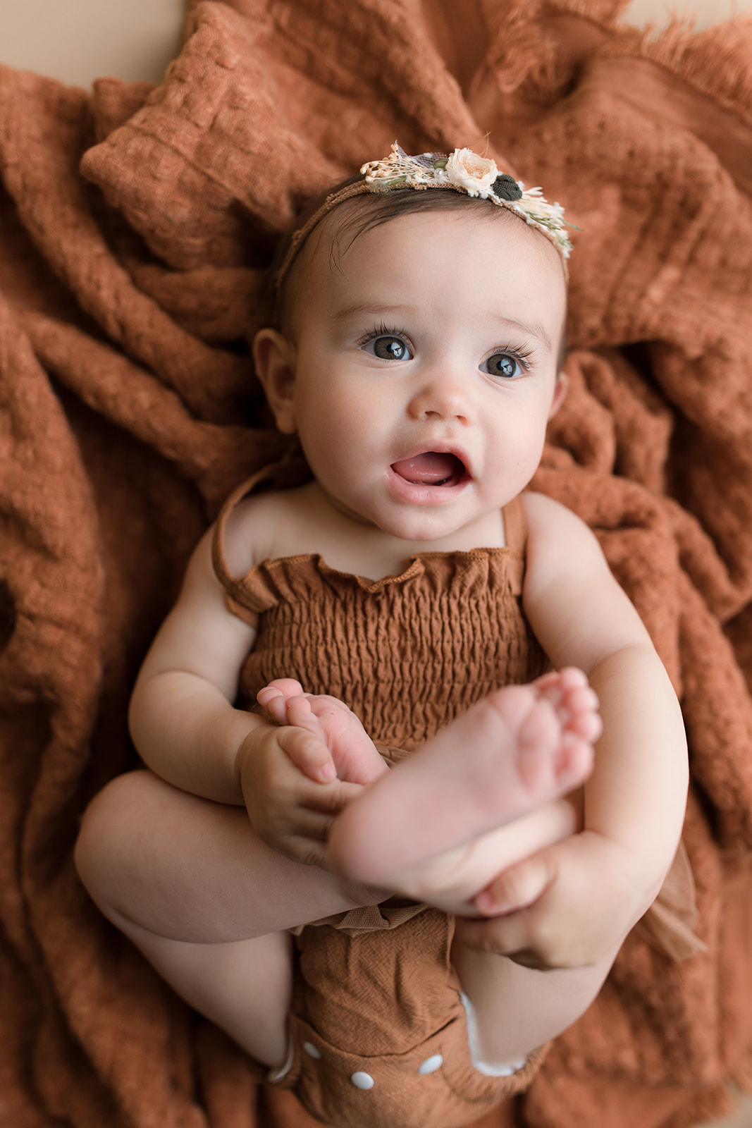 A toddler girl in a brown onesie lays on a blanket with legs up thanks to Fertility Acupuncture Houston