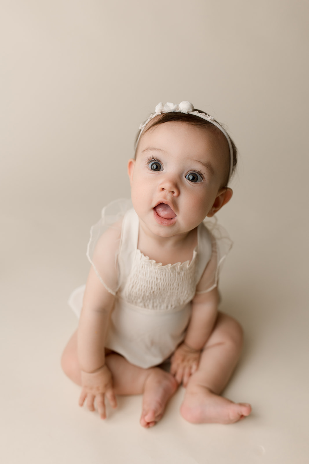 A toddler girl sits on the floor of a studio in a white dress onesie thanks to help from Fertility Acupuncture Houston