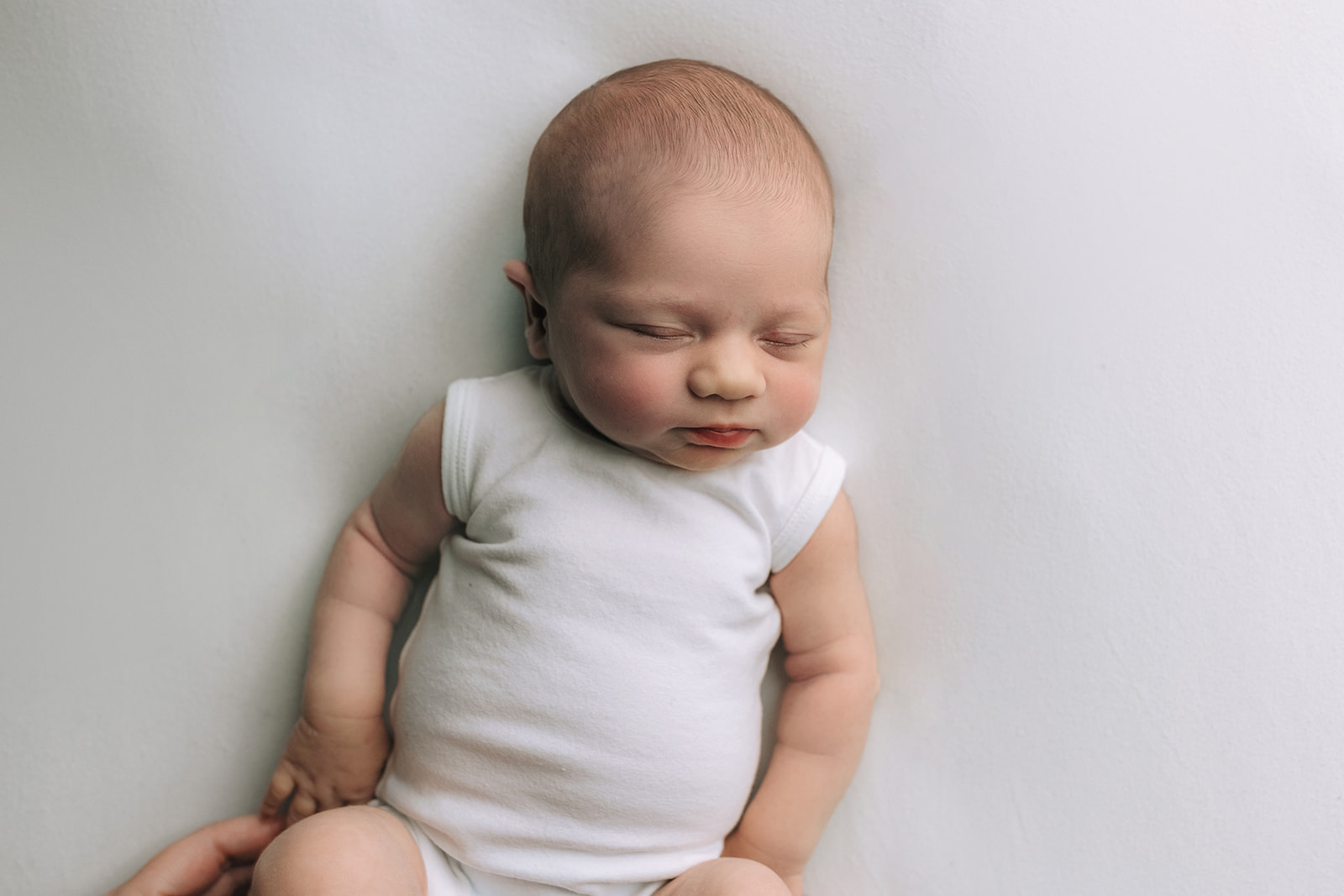 A newborn baby sleeps in a white onesie in a studio after meeting Houston lactation consultants