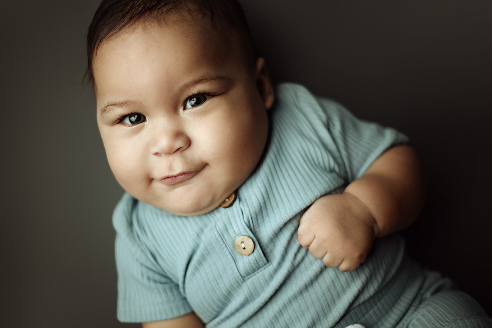 An infant in a blue henley onesie lays in a studio with a smile after visiting Houston Pediatric Dentists