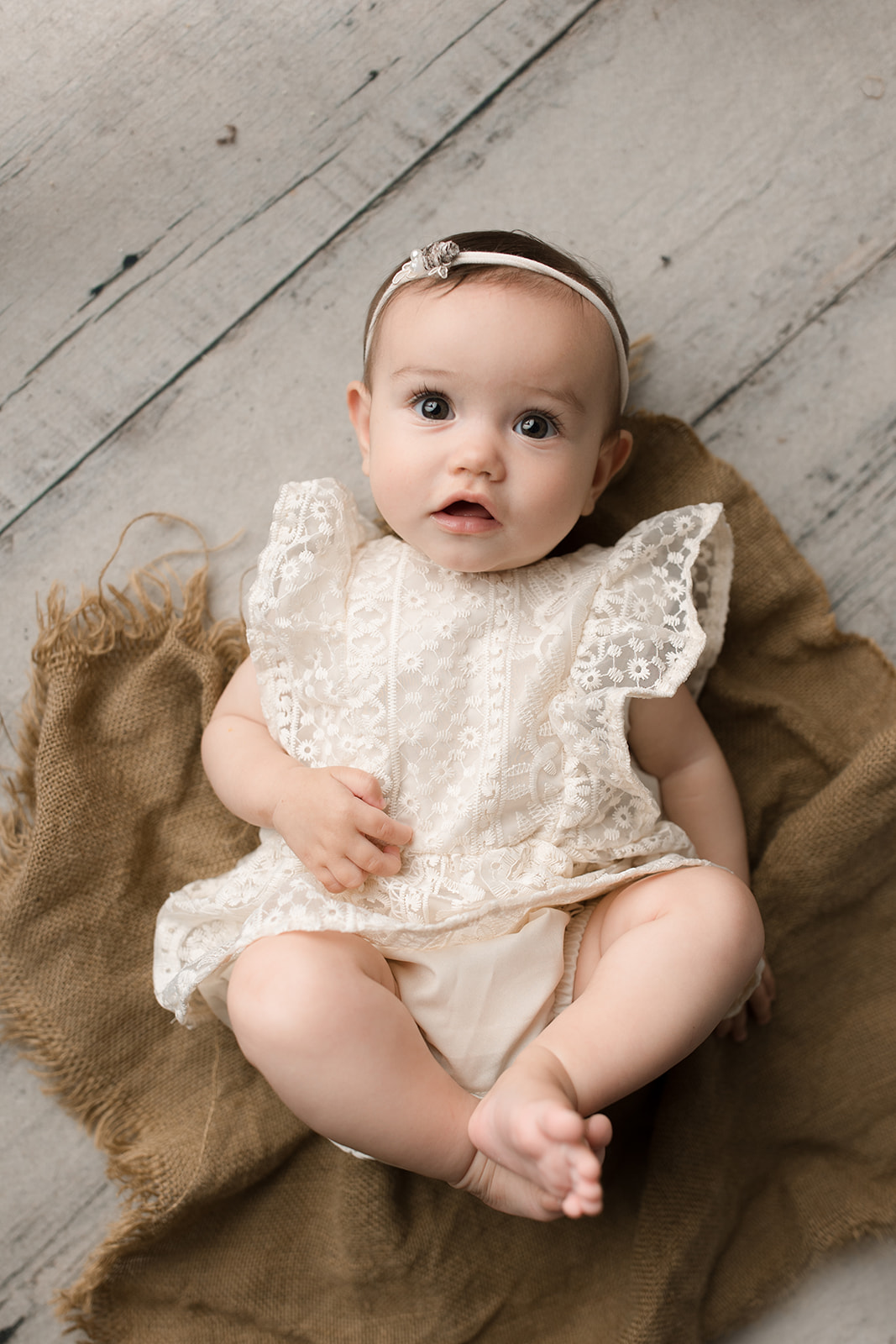 An infant girl in a white lace dress lays on the floor of a studio with eyes open after mom did Houston Prenatal Yoga