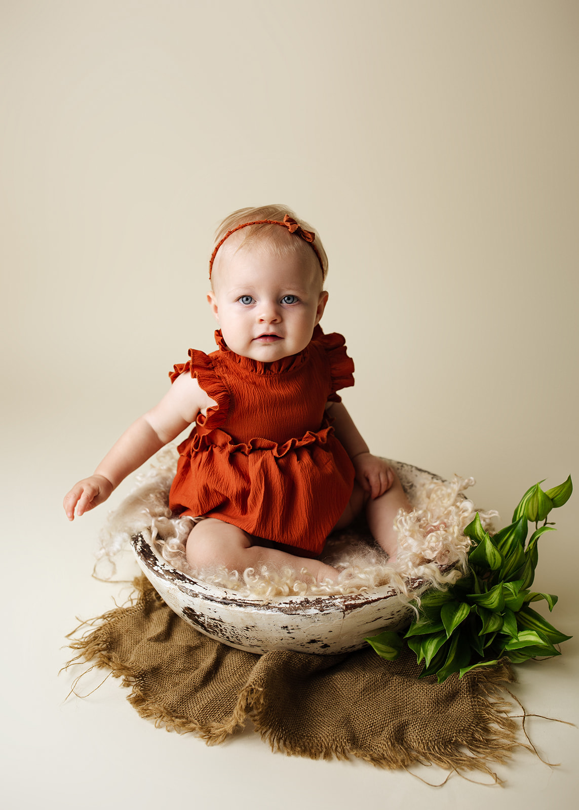 An infant girl in a red dress sits in a wooden bowl in a studio after mom did Houston Prenatal Yoga