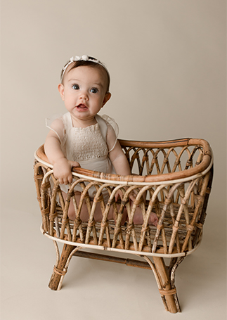 An infant girl sits in a small wicker basket in a studio thanks to an OBGYN In Houston