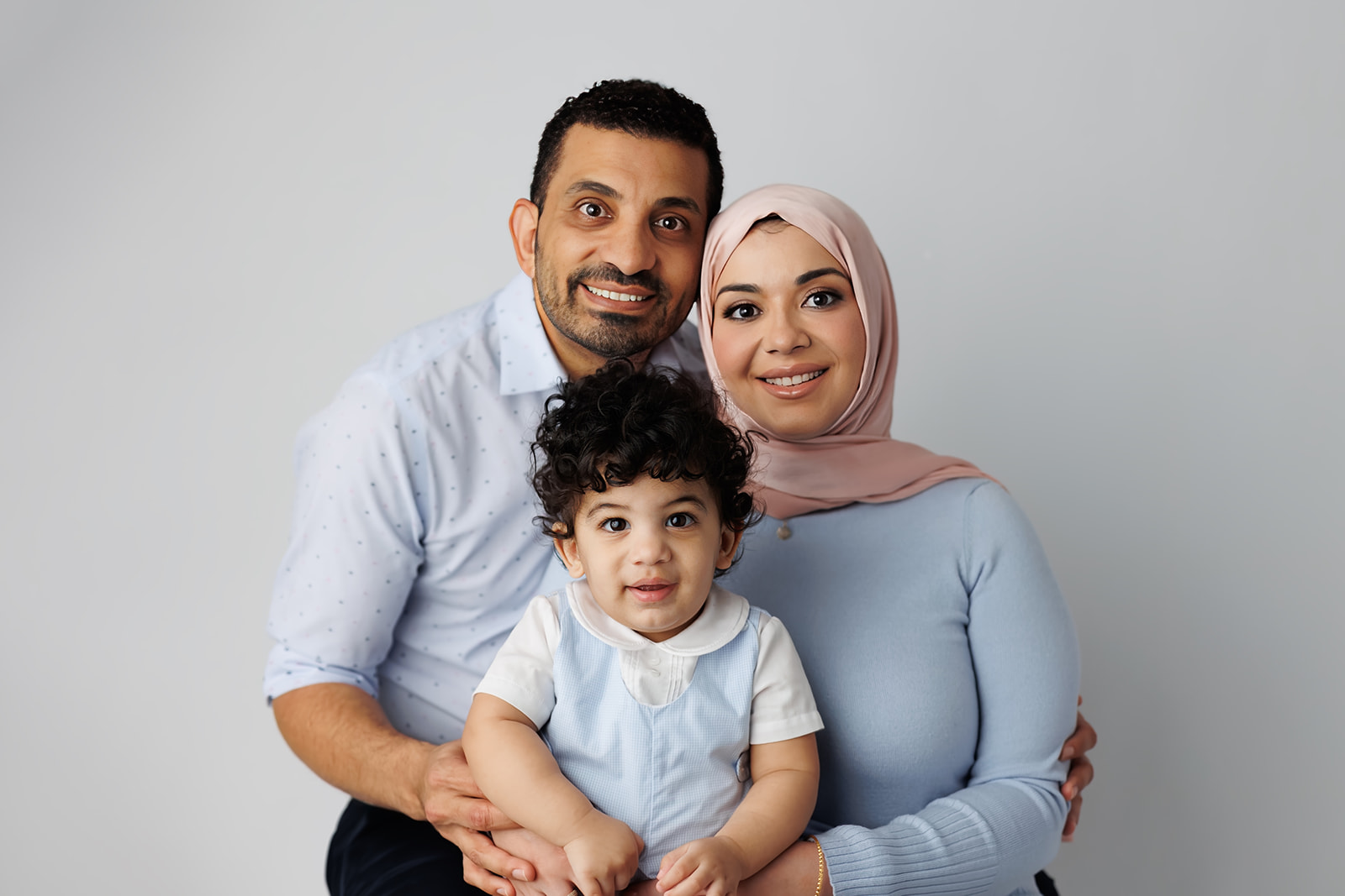 Happy parents stand in a studio in blue with their young toddler in their laps