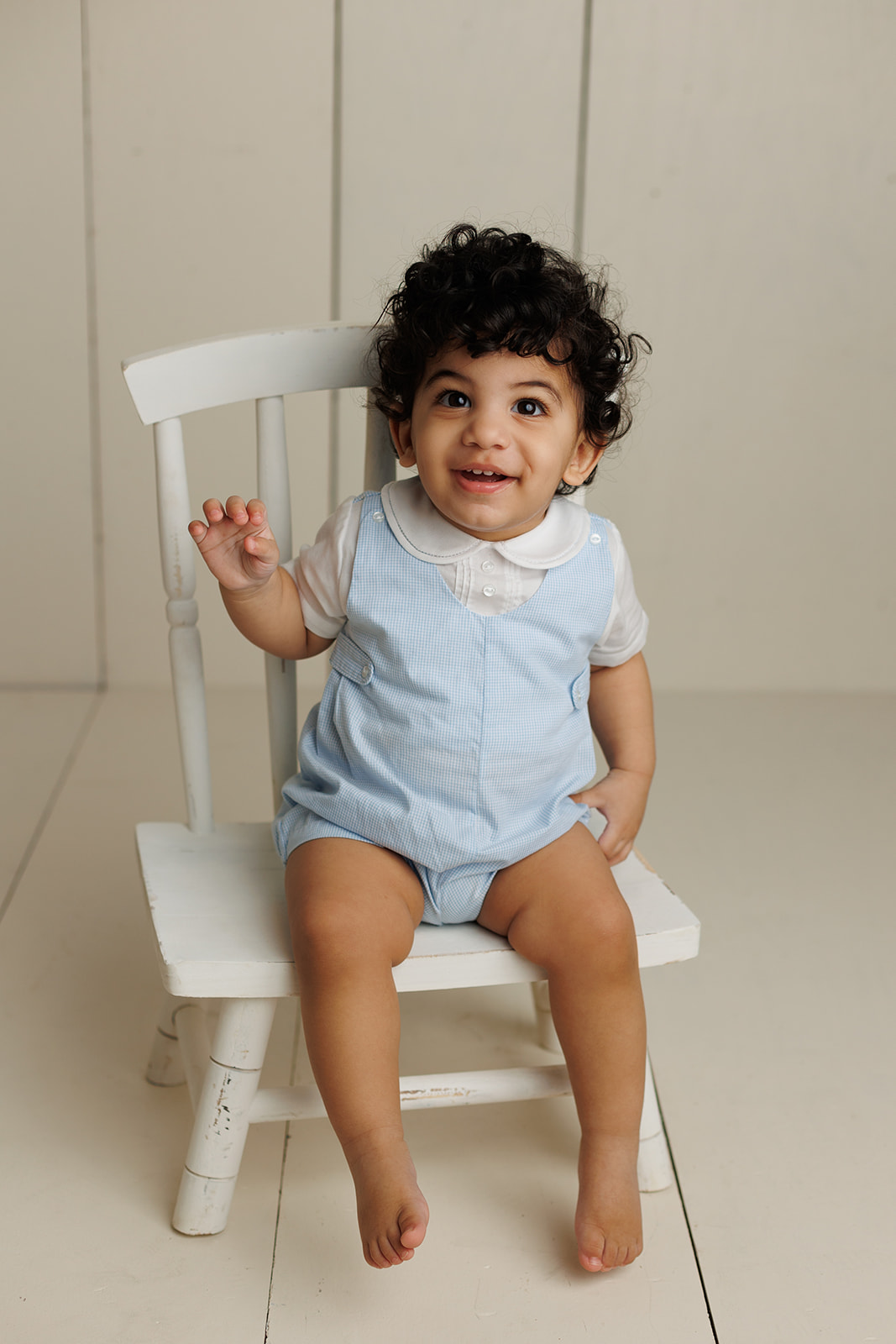 A young toddler in a blue onesie sits on a small wooden chair in a studio thanks to Parenting classes houston