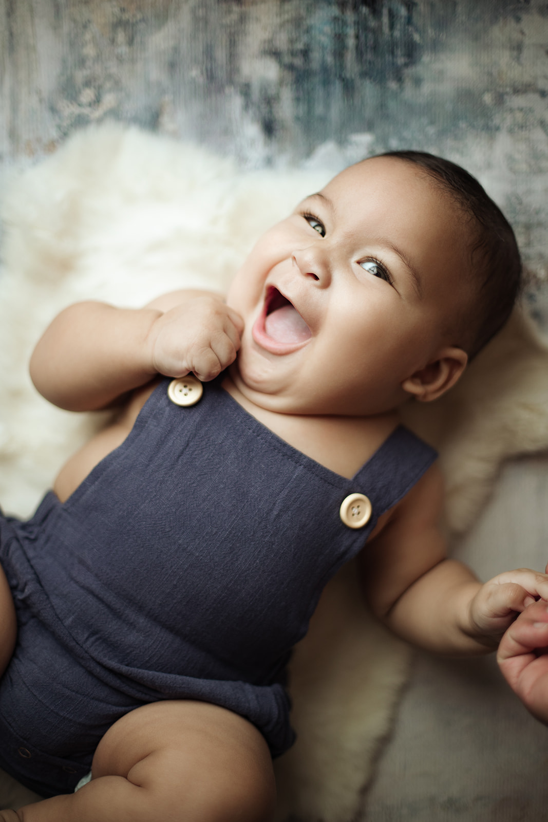 A happy baby lays on a bed in blue overalls after mom visited a Prenatal Chiropractor Houston