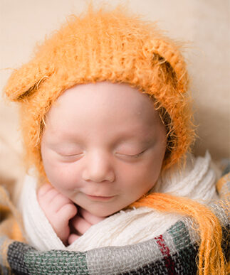 A newborn baby sleeps with a smile in an orange bear ears beanie after mom got some placenta encapsulation houston