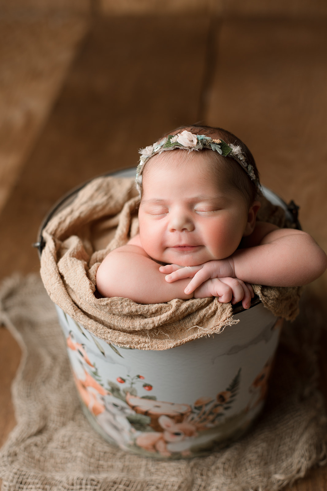 A happy newborn baby sleeps in a tin floral print bucket in a studio after some baby activities Houston