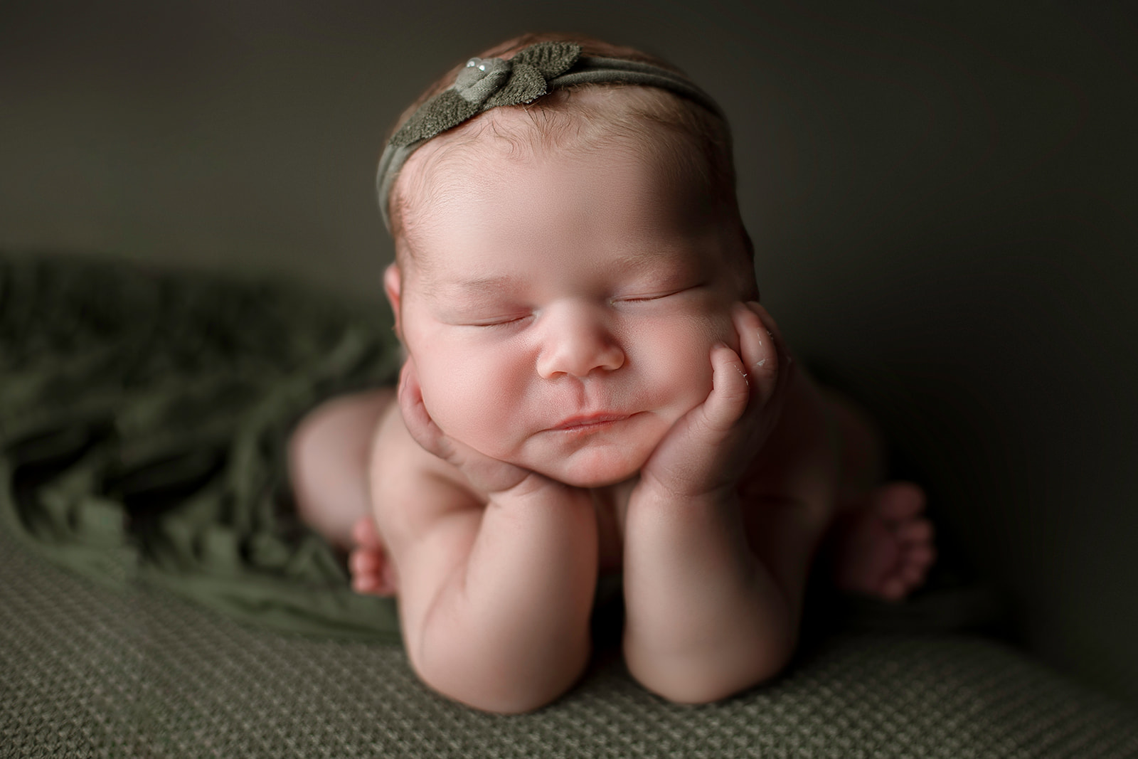 A newborn baby rests her head on her hands while sleeping on a green bed after some baby activities Houston