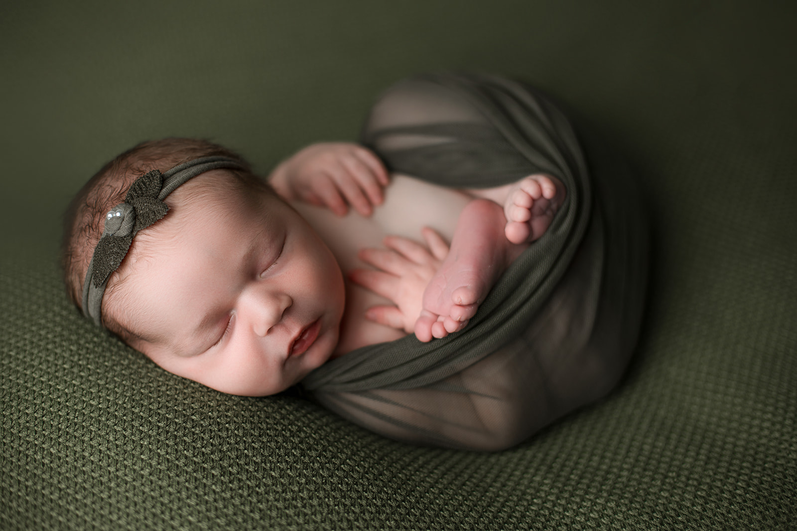 A newborn baby girl sleeps in a green swaddle and matching headband after some Indoor Activities For Toddlers Houston